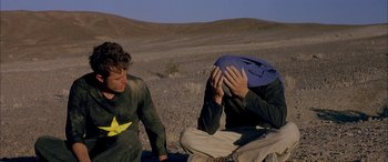 Movie still from “Gerry” (2002), directed by Gus Van Sant – Two men sitting on the ground in the middle of a field; Medium shot, Over the shoulder angle