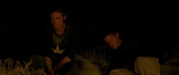 Movie still from “Gerry” (2002), directed by Gus Van Sant – Two men sitting on the ground in the dark; Medium shot, High angle