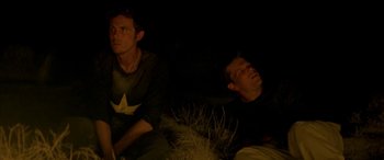 Movie still from “Gerry” (2002), directed by Gus Van Sant – Two men sitting on the ground in the dark; Medium shot, High angle