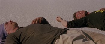 Movie still from “Gerry” (2002), directed by Gus Van Sant – Two people laying on the ground with their hands in the air; Medium shot, Overhead angle