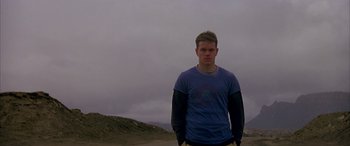 Movie still from “Gerry” (2002), directed by Gus Van Sant – A man standing in the sand with his hands in his pockets; Medium shot, Low angle