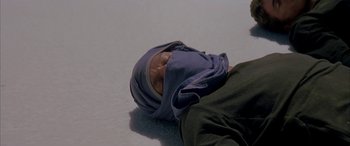 Movie still from “Gerry” (2002), directed by Gus Van Sant – A person laying on the ground wearing a headscarf; Close Up shot, Overhead angle