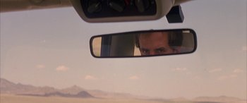 Movie still from “Gerry” (2002), directed by Gus Van Sant – A man is reflected in the rear view mirror of a car; Close Up shot, Over the shoulder angle
