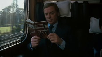 Movie still from “Get Carter” (1971), directed by Mike Hodges – A man in a suit and tie reading a book on a train; Medium shot, High angle