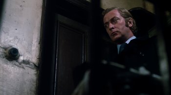 Movie still from “Get Carter” (1971), directed by Mike Hodges – A person wearing a suit near a door; Close Up shot, Low angle