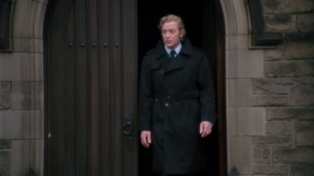 Movie still from “Get Carter” (1971), directed by Mike Hodges – A man in a black coat and tie standing in front of a door; Medium shot, Low angle