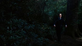 Movie still from “Get Carter” (1971), directed by Mike Hodges – A man in a suit and sunglasses walking through the woods; Wide shot, High angle