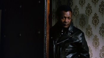 Movie still from “Get Carter” (1971), directed by Mike Hodges – A man in a leather jacket standing in front of a mirror; Medium shot, Low angle