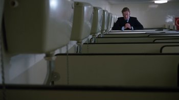 Movie still from “Get Carter” (1971), directed by Mike Hodges – A man sitting in a row of cubicles; Wide shot, Low angle