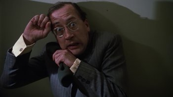 Movie still from “Get Carter” (1971), directed by Mike Hodges – A man in a suit and glasses leaning against a wall; Close Up shot, Low angle