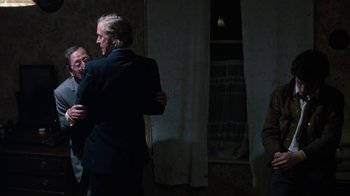 Movie still from “Get Carter” (1971), directed by Mike Hodges – A man in a black suit is hugging another man in front of a window; Medium shot, Over the shoulder angle