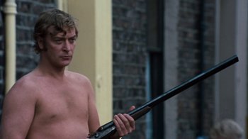 Movie still from “Get Carter” (1971), directed by Mike Hodges – A shirtless man holding a gun in his hand; Medium shot, Over the shoulder angle