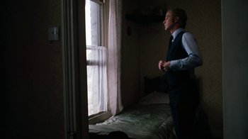 Movie still from “Get Carter” (1971), directed by Mike Hodges – A man standing in front of a window looking outside; Medium shot, Low angle