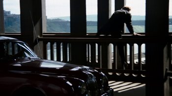Movie still from “Get Carter” (1971), directed by Mike Hodges – A man sitting on top of a wooden railing next to a car; Wide shot, High angle
