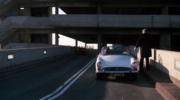 Movie still from “Get Carter” (1971), directed by Mike Hodges – A white car driving down a street under a bridge; Wide shot, Over the shoulder angle