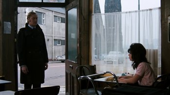 Movie still from “Get Carter” (1971), directed by Mike Hodges – A woman sitting at a table in front of an open door; Wide shot, Over the shoulder angle