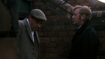 Movie still from “Get Carter” (1971), directed by Mike Hodges – Two men standing next to each other in front of a brick wall; Medium shot, Over the shoulder angle