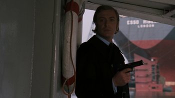 Movie still from “Get Carter” (1971), directed by Mike Hodges – A man holding a gun standing in front of a window; Medium shot, Low angle
