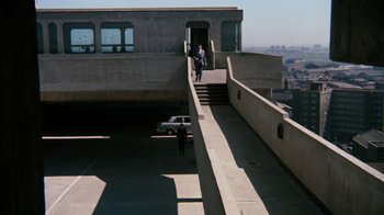 Movie still from “Get Carter” (1971), directed by Mike Hodges – Two people walking up a ramp to a car; Extreme Wide shot, High angle