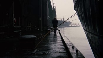 Movie still from “Get Carter” (1971), directed by Mike Hodges – A man standing next to a boat on the water; Extreme Wide shot, High angle