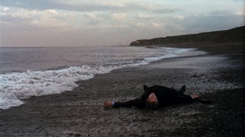 Movie still from “Get Carter” (1971), directed by Mike Hodges – A person laying on the beach in the sand; Wide shot, High angle