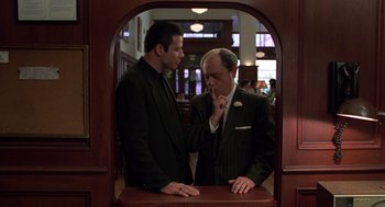 Movie still from “Get Shorty” (1995), directed by Barry Sonnenfeld – A couple of men standing next to each other in a room; Medium shot, Over the shoulder angle