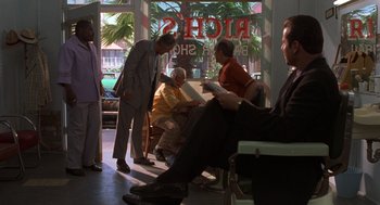 Movie still from “Get Shorty” (1995), directed by Barry Sonnenfeld – A group of people sitting in a room with palm trees in the background; Wide shot, Over the shoulder angle