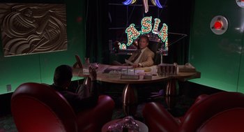 Movie still from “Get Shorty” (1995), directed by Barry Sonnenfeld – A man sitting at a table in front of a neon sign; Wide shot, High angle