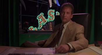 Movie still from “Get Shorty” (1995), directed by Barry Sonnenfeld – A man sitting at a table in front of a neon sign; Medium shot, Low angle