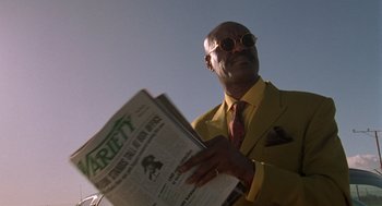 Movie still from “Get Shorty” (1995), directed by Barry Sonnenfeld – A man in a yellow suit holding a newspaper in his hands; Close Up shot, Low angle