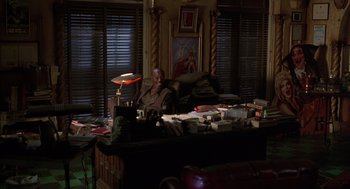 Movie still from “Get Shorty” (1995), directed by Barry Sonnenfeld – A man sitting at a cluttered desk in a living room; Wide shot, High angle