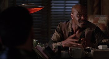 Movie still from “Get Shorty” (1995), directed by Barry Sonnenfeld – A man sitting at a table with a cup in front of him; Medium shot, Over the shoulder angle