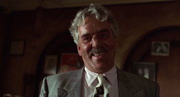 Movie still from “Get Shorty” (1995), directed by Barry Sonnenfeld – An older man in a suit and tie smiling for the camera; Close Up shot, Low angle