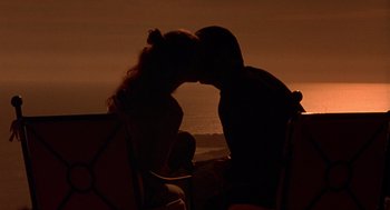 Movie still from “Get Shorty” (1995), directed by Barry Sonnenfeld – Two people sitting on a chair kissing at the beach; Medium shot, Low angle