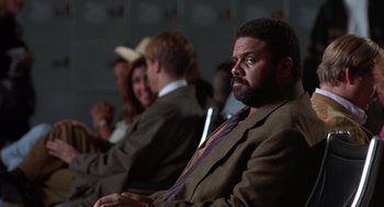 Movie still from “Get Shorty” (1995), directed by Barry Sonnenfeld – A man in a suit sitting in front of a group of people; Close Up shot, Over the shoulder angle