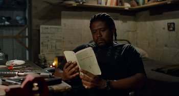Movie still from “Ghost Dog: The Way of the Samurai” (1999), directed by Jim Jarmusch – A man sitting at a table reading a book; Medium shot, High angle