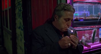 Movie still from “Ghost Dog: The Way of the Samurai” (1999), directed by Jim Jarmusch – A man in a suit smoking a cigarette in front of a red wall; Medium shot, Low angle
