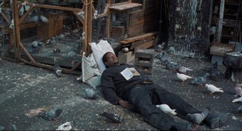 Movie still from “Ghost Dog: The Way of the Samurai” (1999), directed by Jim Jarmusch – A man laying on the ground surrounded by pigeons; Wide shot, High angle