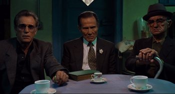 Movie still from “Ghost Dog: The Way of the Samurai” (1999), directed by Jim Jarmusch – An older man sitting at a table with a book; Medium shot, Low angle