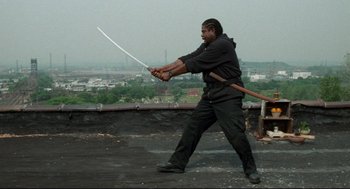 Movie still from “Ghost Dog: The Way of the Samurai” (1999), directed by Jim Jarmusch – A man is holding a sword in his hand; Medium shot, Low angle