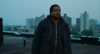 Movie still from “Ghost Dog: The Way of the Samurai” (1999), directed by Jim Jarmusch – A man standing on top of a building in front of a city; Medium shot, Low angle
