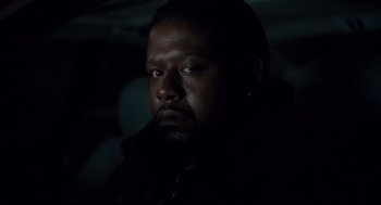 Movie still from “Ghost Dog: The Way of the Samurai” (1999), directed by Jim Jarmusch – A man in a dark room looking at the camera; Close Up shot, Over the shoulder angle