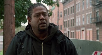 Movie still from “Ghost Dog: The Way of the Samurai” (1999), directed by Jim Jarmusch – A person sitting on a bench near a building; Close Up shot, Over the shoulder angle