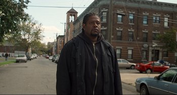 Movie still from “Ghost Dog: The Way of the Samurai” (1999), directed by Jim Jarmusch – A man standing on the side of the road in front of a building; Medium shot, Low angle