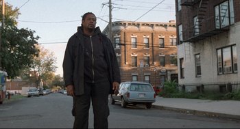 Movie still from “Ghost Dog: The Way of the Samurai” (1999), directed by Jim Jarmusch – A man standing on the side of the road in front of a building; Wide shot, Low angle