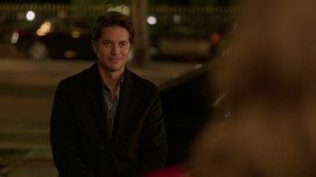 Movie still from “Emily in Paris” (2020), created by Darren Star – A man in a black suit is smiling for the camera; Close Up shot, Over the shoulder angle