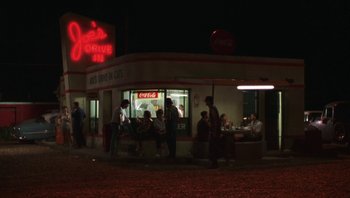 Movie still from “Ghosts of Mississippi” (1996), directed by Rob Reiner – A group of people standing outside of a restaurant at night; Extreme Wide shot, High angle