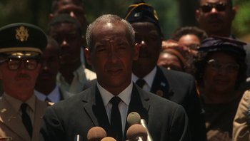 Movie still from “Ghosts of Mississippi” (1996), directed by Rob Reiner – A man in a black suit and a microphone; Close Up shot, Low angle