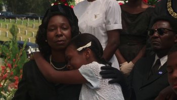 Movie still from “Ghosts of Mississippi” (1996), directed by Rob Reiner – A woman and a girl are hugging in front of a group of people; Medium shot, Low angle