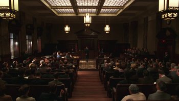 Movie still from “Ghosts of Mississippi” (1996), directed by Rob Reiner – People are sitting in a courtroom with a speaker; Extreme Wide shot, High angle